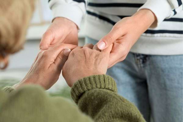 Une personne réconforte une autre en lui tenant doucement les mains.