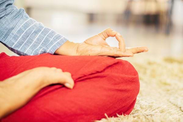 Personne assise en tailleur, main en mudra sur le genou.