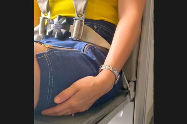 Zoom sur la main d&rsquo;une h&ocirc;tesse gliss&eacute;e sous sa cuisse, ceintur&eacute;e.