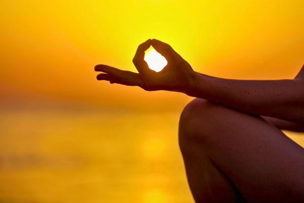 Main en mudra devant un coucher de soleil.