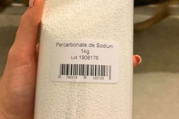 Main tenant un pot de percarbonate de sodium de 1 kg.