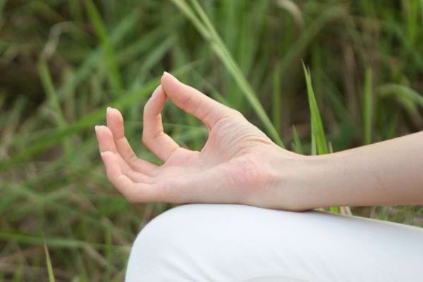 Main en mudra posée sur un genou, herbe en fond.