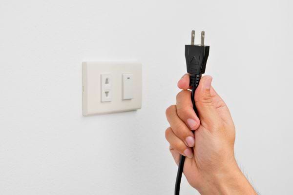 Une main tient une prise prête à être branchée.