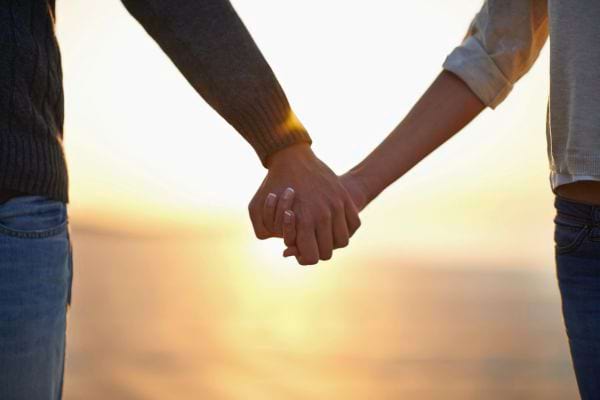 Deux personnes se tiennent la main face au coucher de soleil.