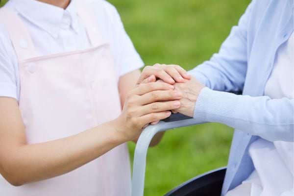 Une infirmière tient tendrement les mains d'une personne âgée en fauteuil roulant.