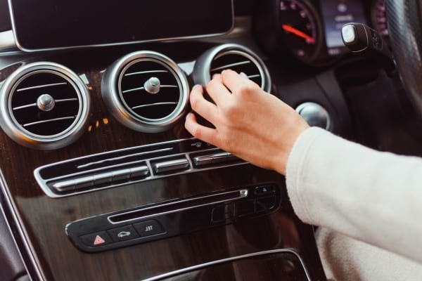 Une main oriente les bouches d’aération sur le tableau de bord d’une voiture.