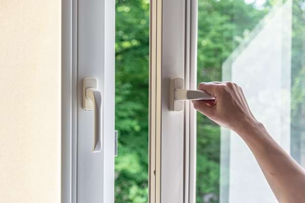 Main ouvrant une fenêtre donnant sur la nature.