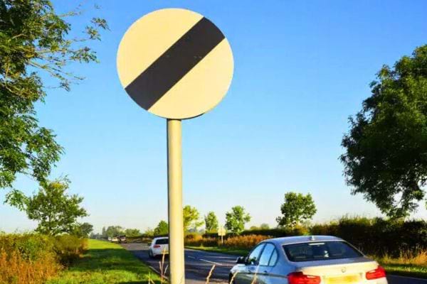 Panneau rond blanc à bande noire sur route de campagne.