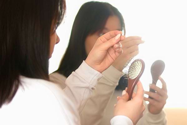 Femme observant des cheveux perdus dans sa brosse.