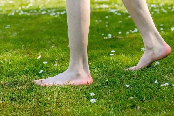 Une personne marche pieds nus sur une pelouse avec des pâquerettes.