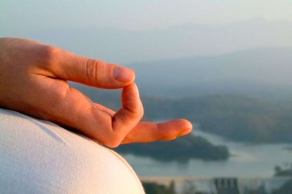 Main en mudra au-dessus d’un paysage de montagne.