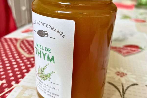 Pot de miel de thym posé sur une nappe colorée.