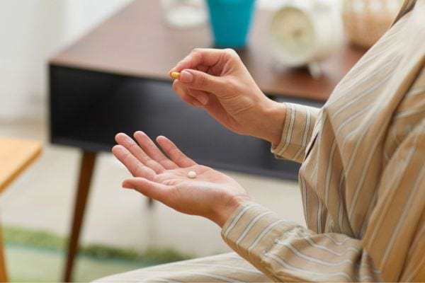 Femme tenant des compléments alimentaires dans la main.