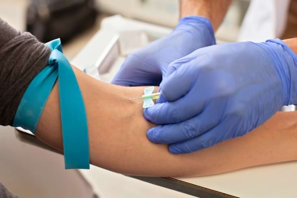 Prise de sang en cours avec des gants médicaux bleus.