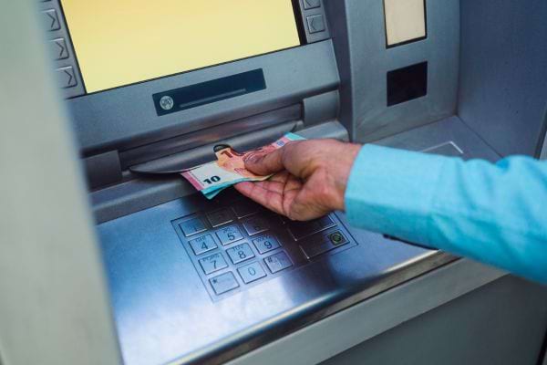 Un homme prend un billet de 10 € au distributeur.