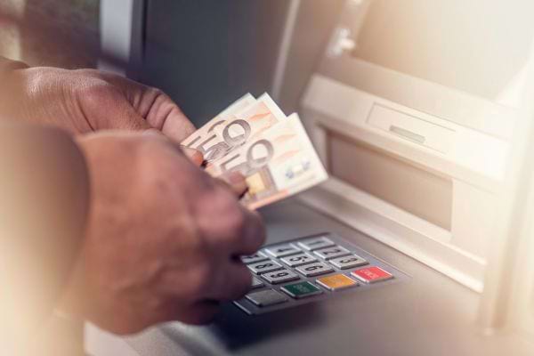 Une personne retire plusieurs billets de 50 € à un distributeur automatique.