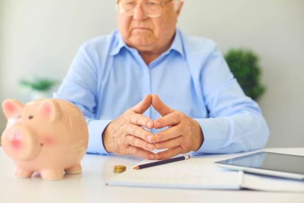 Un homme âgé assis devant une tirelire et des papiers.