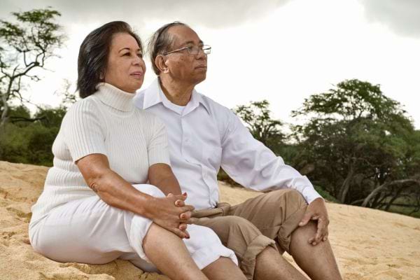 Un couple âgé assis sur la plage regarde l’horizon.