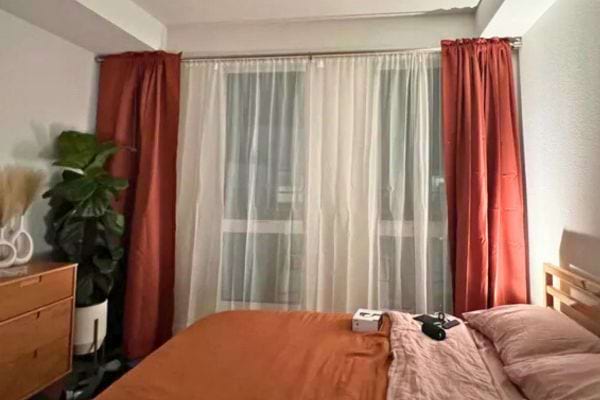 Chambre avec lit orange et rideaux tirés.