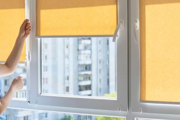 Personne abaissant un store occultant sur une fenêtre.