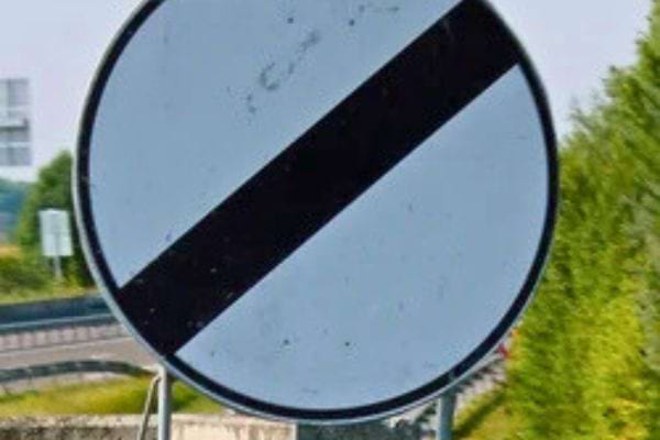 Gros plan d’un panneau blanc rayé noir en bord d’autoroute.