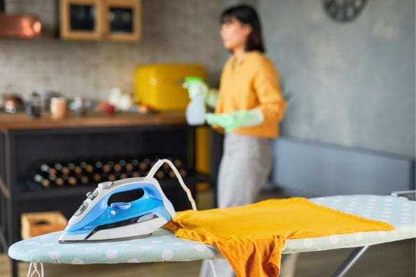 Fer à repasser posé sur une planche avec un t-shirt orange.