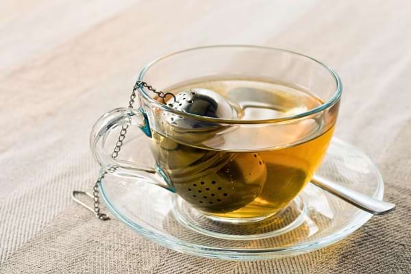 Tasse de thé avec infuseur en métal et cuillère posée sur la soucoupe.