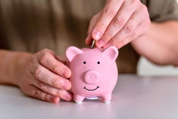 Une pièce est insérée dans une tirelire rose souriante.