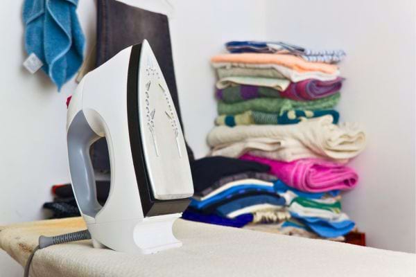 Fer à repasser devant une pile de linge plié.