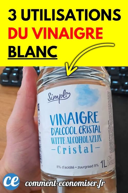 Une main tenant une bouteille de vinaigre blanc d’alcool cristal devant un clavier d’ordinateur noir.