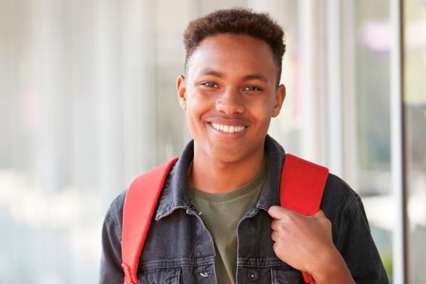 Jeune homme souriant avec un sac à dos rouge, illustrant la jeunesse, la mobilité ou les vacances.