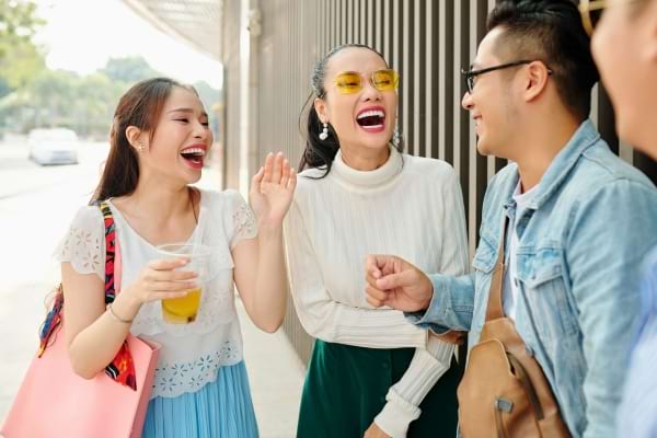 Trois amis asiatiques rient aux éclats en discutant dans la rue, boisson à la main.