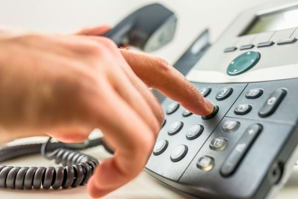 Une main compose un numéro d'urgence sur un téléphone fixe.