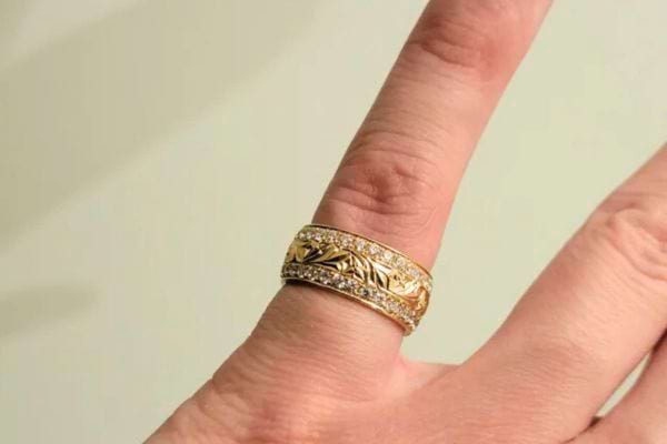 Bague dorée large et travaillée sur le petit doigt.