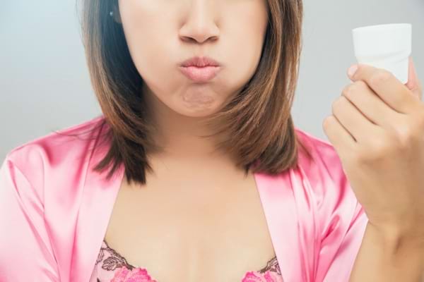 Une femme en peignoir rose fait un bain de bouche en gonflant ses joues.