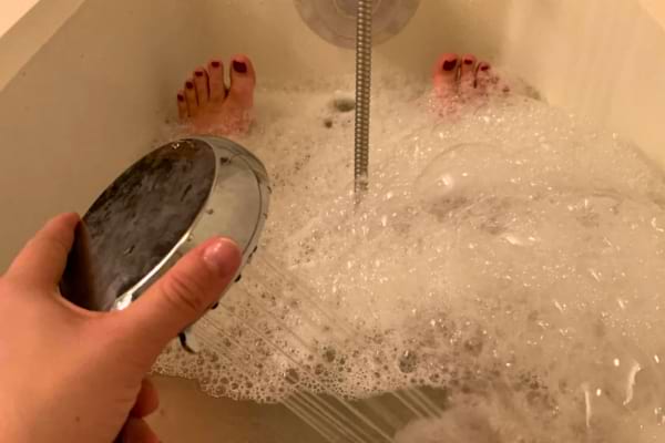 Une personne prend un bain moussant, arrose ses jambes avec un pommeau de douche.