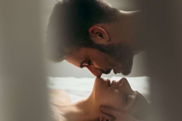 Homme s’apprêtant à embrasser sa partenaire au lit.