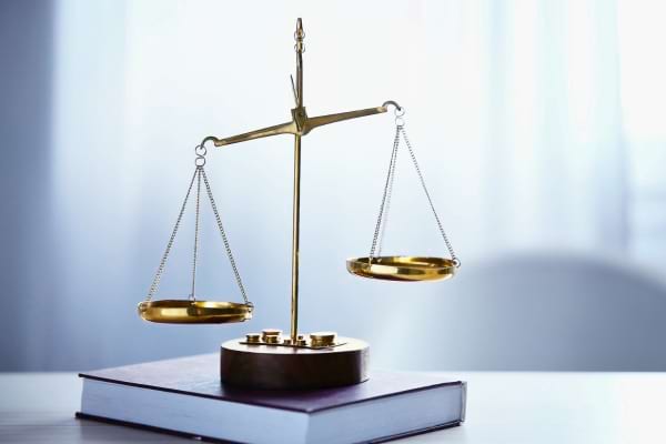 Balance dorée déséquilibrée posée sur un gros livre fermé.