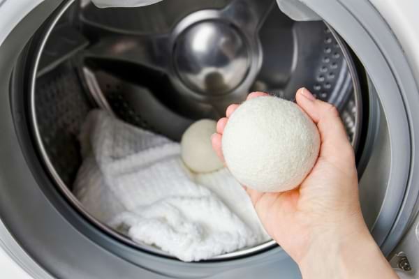Une main tient une balle de laine devant un sèche-linge rempli de serviettes blanches.