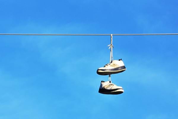 Des baskets blanches suspendues à un fil au-dessus d’une rue, ciel bleu en fond.