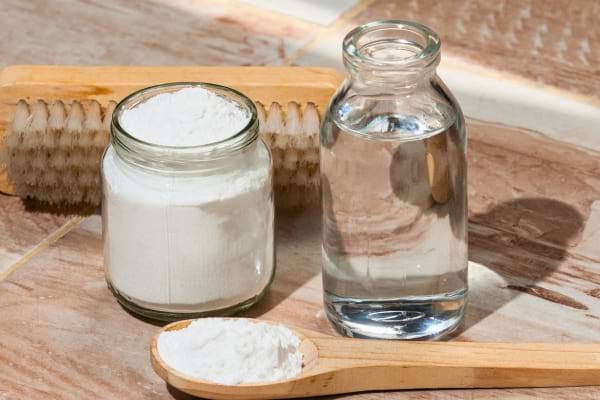 Bicarbonate et vinaigre blanc posés près d’une brosse sur un sol, prêts pour le nettoyage naturel.