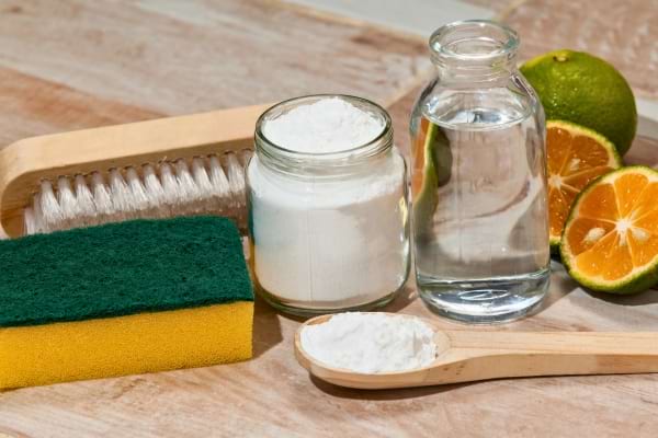 Bicarbonate, vinaigre, éponge et agrumes réunis sur un plan de travail, parfaits pour une recette de nettoyant maison.