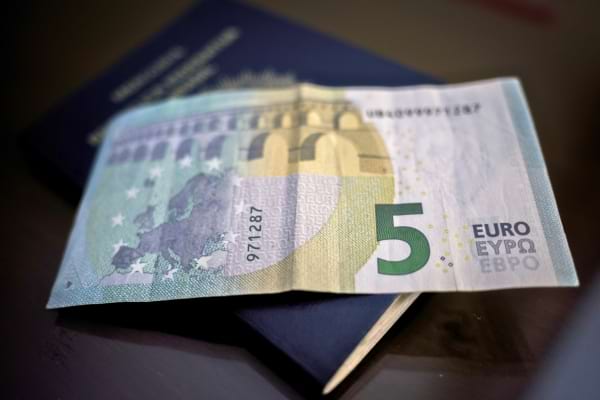 Un billet de 5 euros posé sur un passeport bleu foncé, évoquant les petites dépenses.