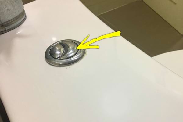 Une flèche jaune pointe vers le petit bouton de la chasse d’eau.