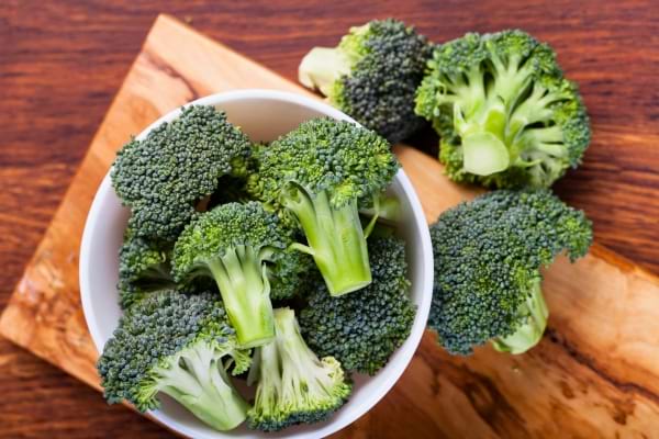 Petits bouquets de brocolis frais dans un bol blanc sur planche bois.
