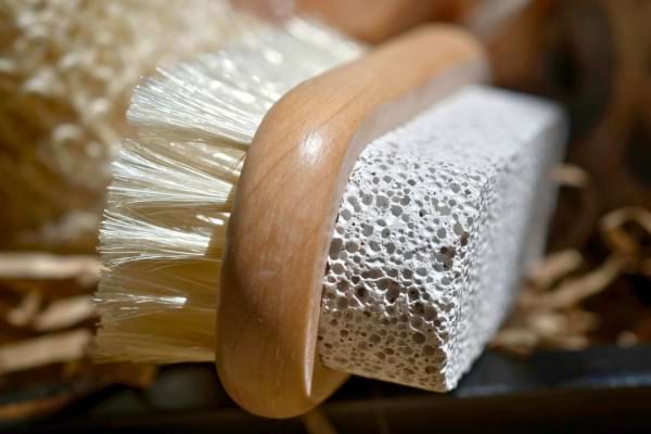 Grosse brosse en bois avec pierre ponce, posée parmi d'autres accessoires de bain.