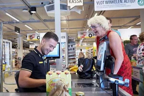 Un caissier discute avec une cliente âgée souriante.