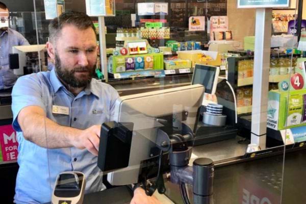 Un caissier scanne un produit derrière un plexiglas.