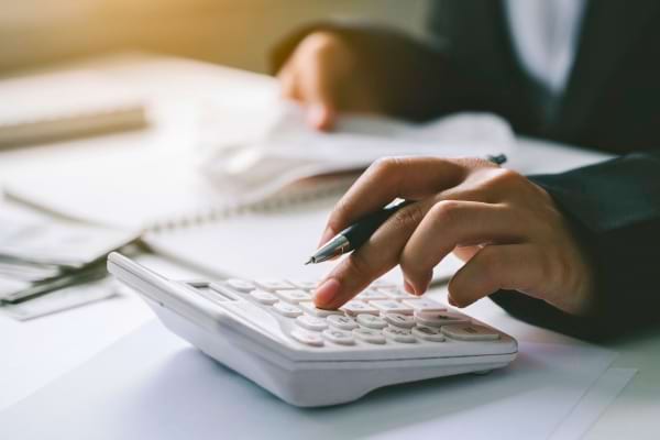 Main appuyant sur une calculatrice avec un stylo, symbolisant la gestion ou vérification des dépenses.