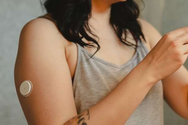 Femme portant un capteur de glycémie fixé à l’arrière de son bras gauche.
